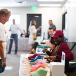 A photo of a man at a booth with hats talking to a woman