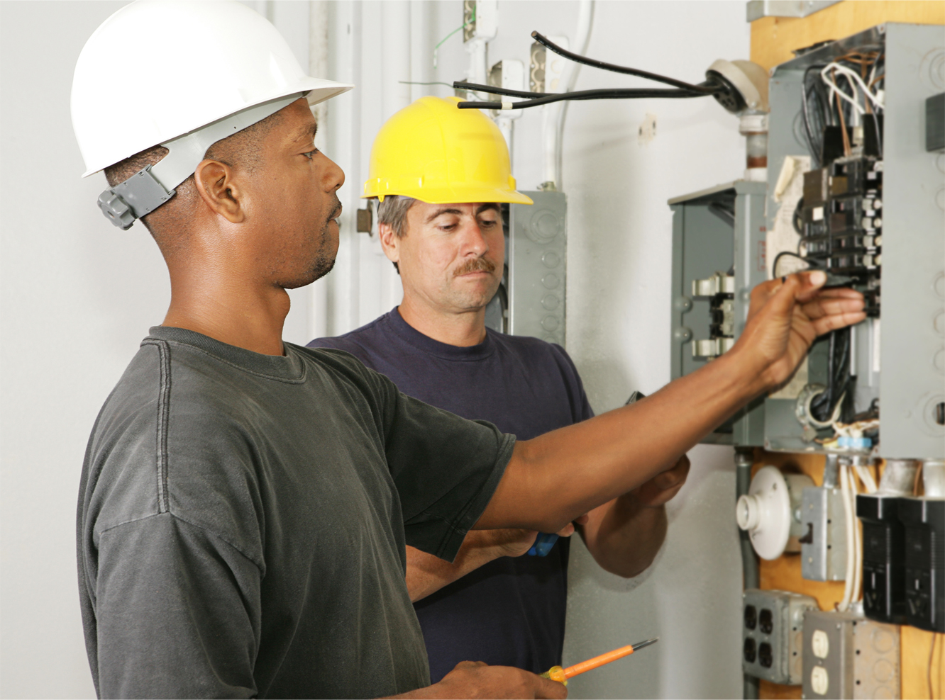 Photograph of two electricians working on a power panel.