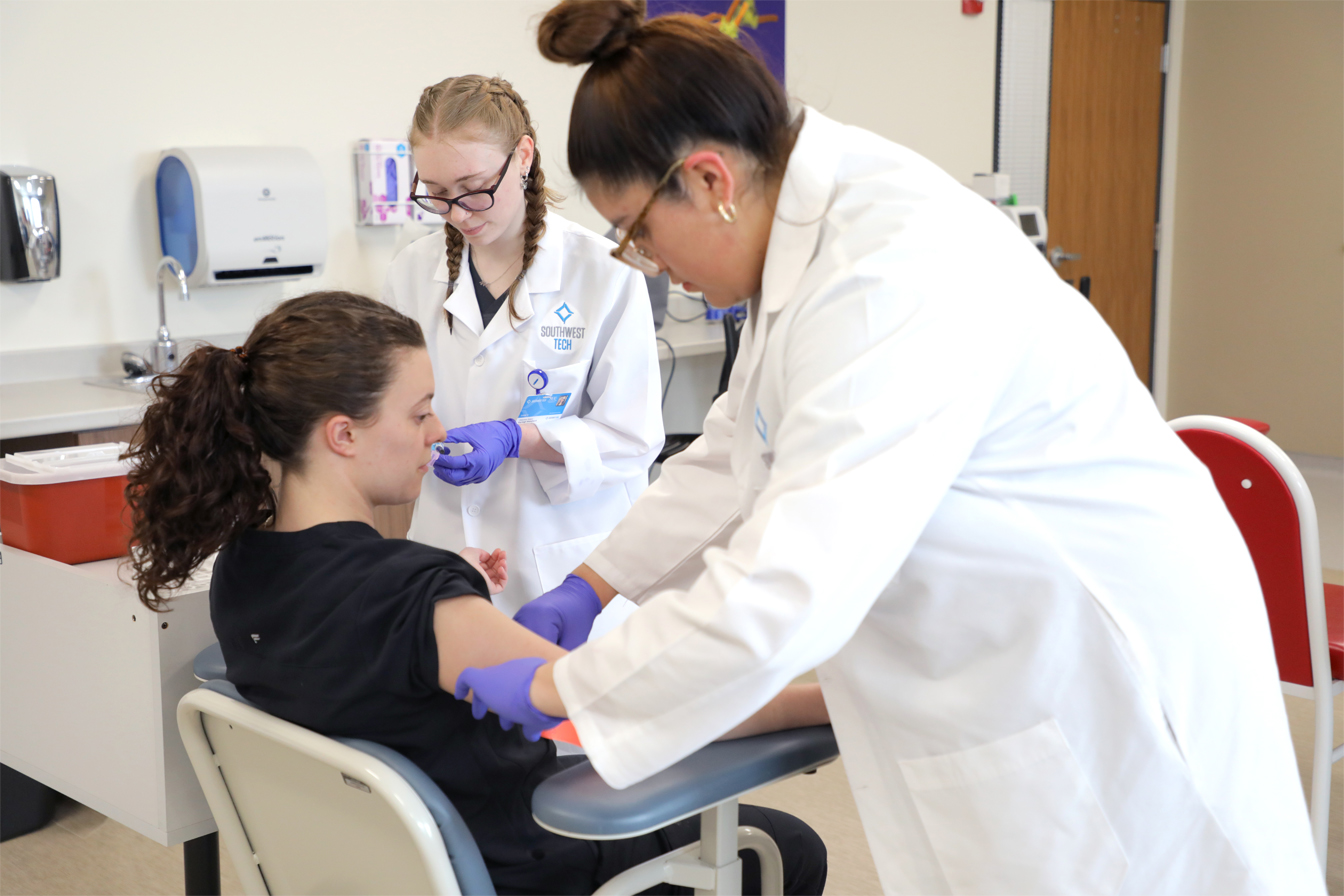 Photograph of Health profession students prepping an individual for a blood draw.