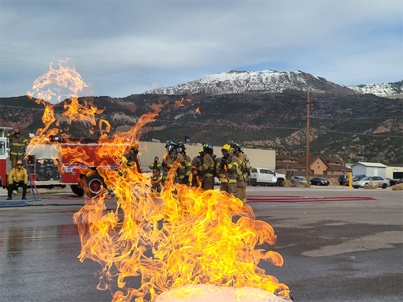 firefighter students doing a drill with a small fire burning near them.