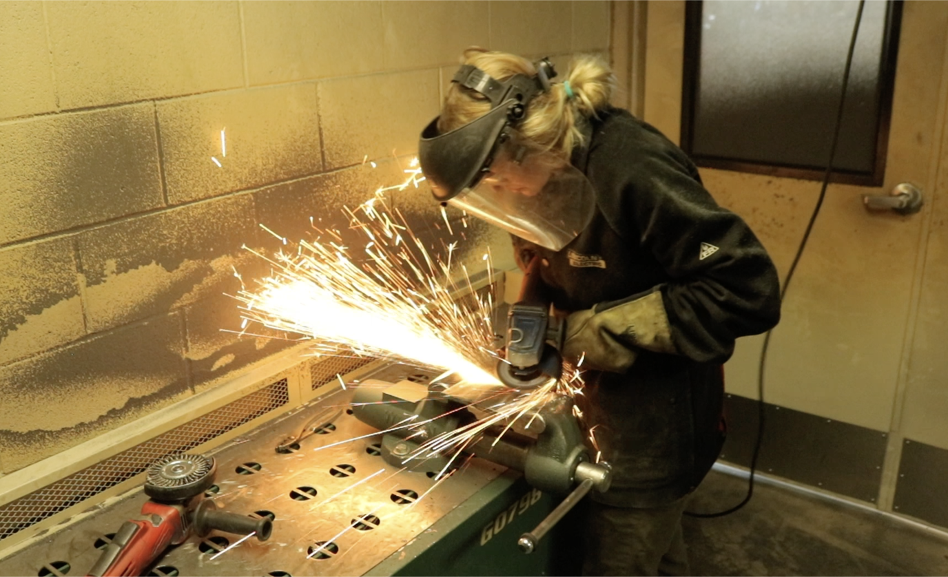 Photograph of a student grinding a piece of metal with a power tool.