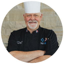 Chef Jon Woodgate in a white toque and black chef's coat, arms crossed.