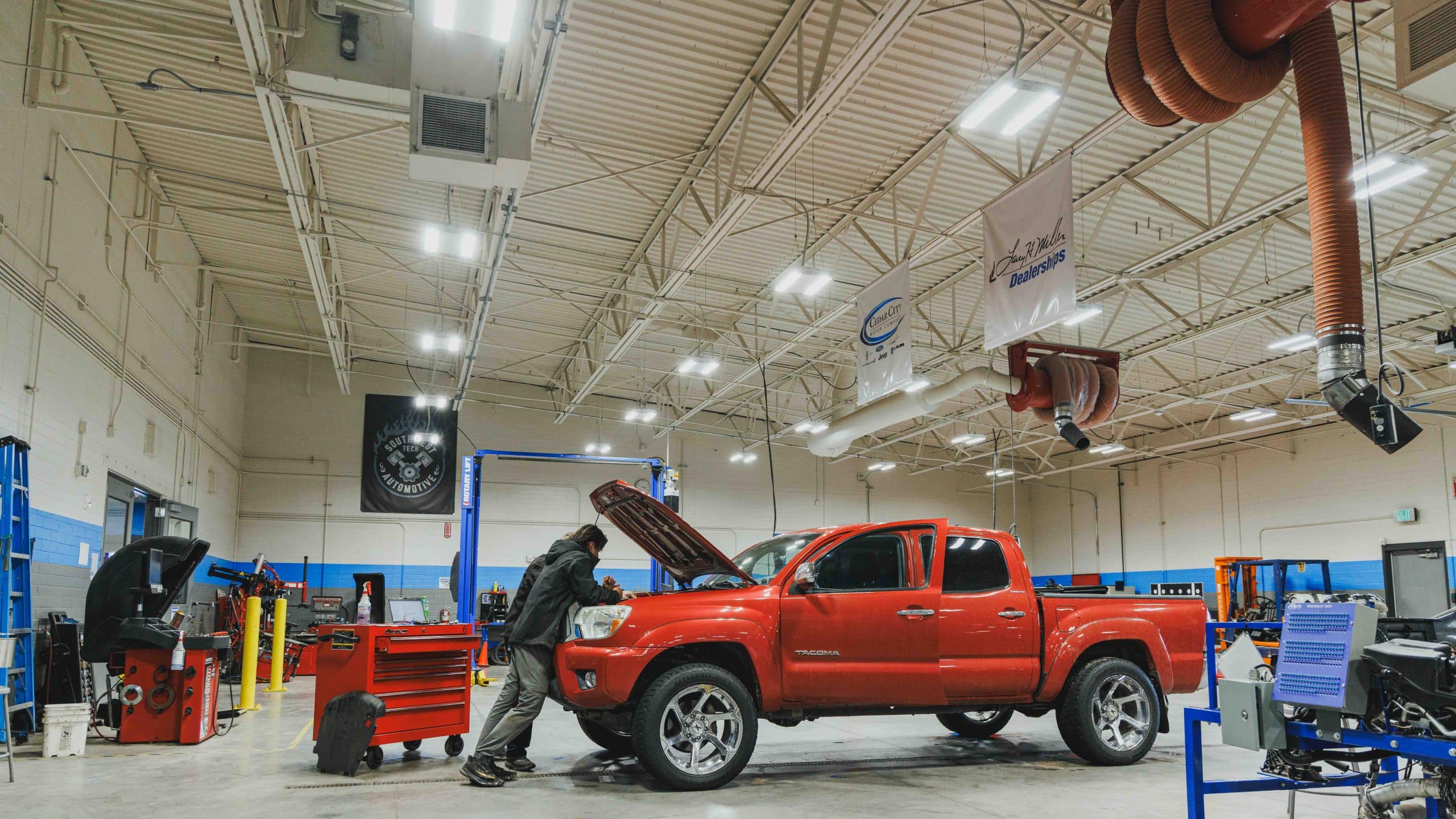Student works under the hood of a red pickup in an automotive shop.